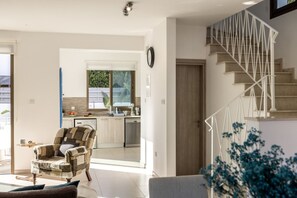 A modern living room with a stone-patterned armchair, a sofa, and a staircase with a white railing. - Stylish Villa | Private Pool - Garden - Near Beach (Paralimni)