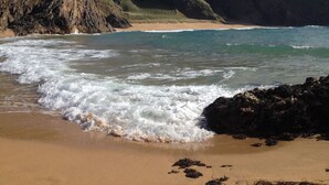 Ein Strand mit Wellen, felsigen Klippen und blauem Himmel.