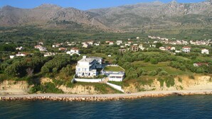 A coastal town with a prominent white building with a balcony, surrounded by greenery and mountains in the background. - Cliff Bay Hotel by GHH (Aktio-Vonitsa)