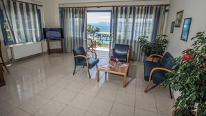 A hotel room with a view of the sea, a television, a wooden table with magazines, and two blue chairs. - Cliff Bay Hotel by GHH (Aktio-Vonitsa)