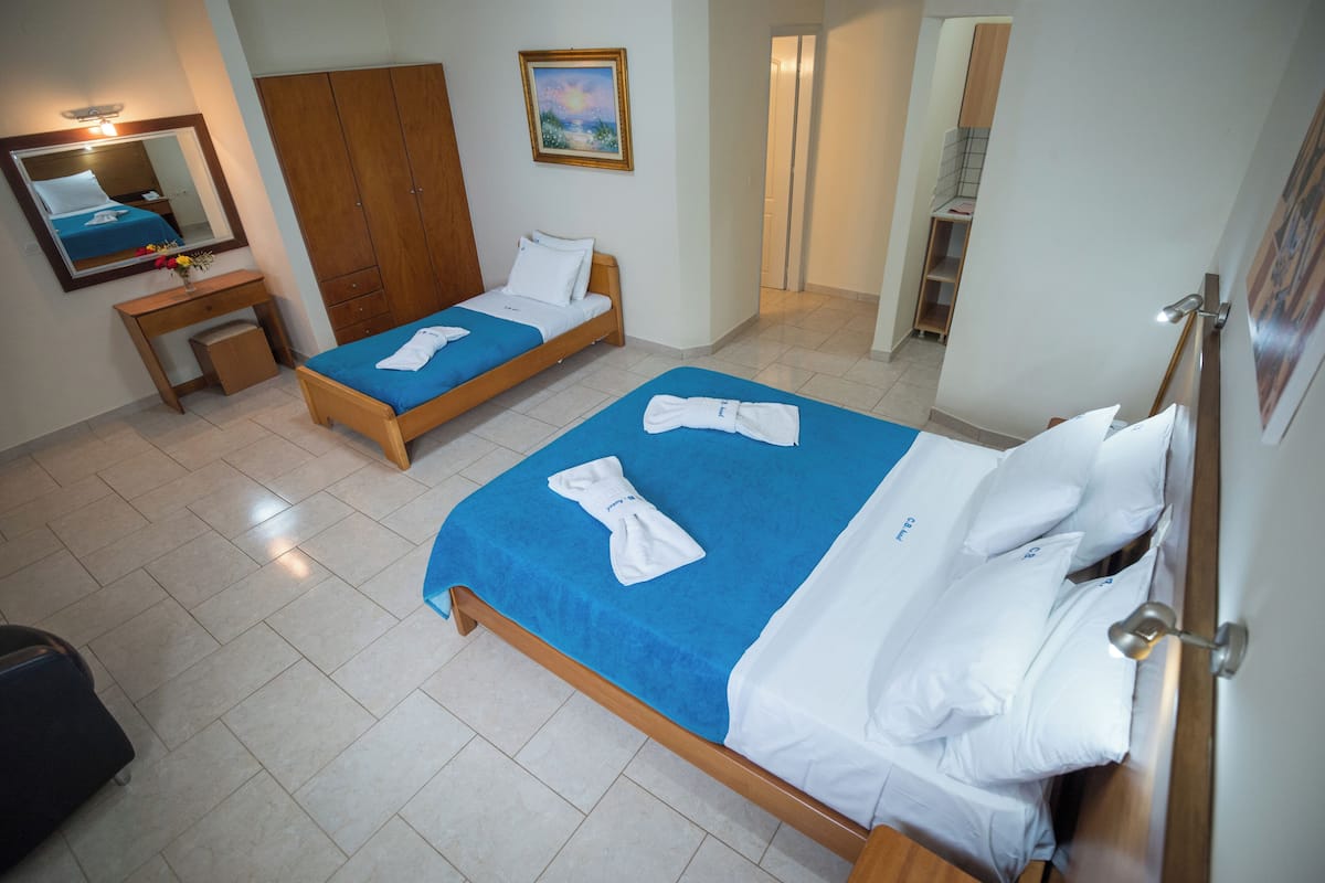 A hotel room with two beds, a wooden wardrobe, a desk with a mirror, and a bathroom visible through an open door.