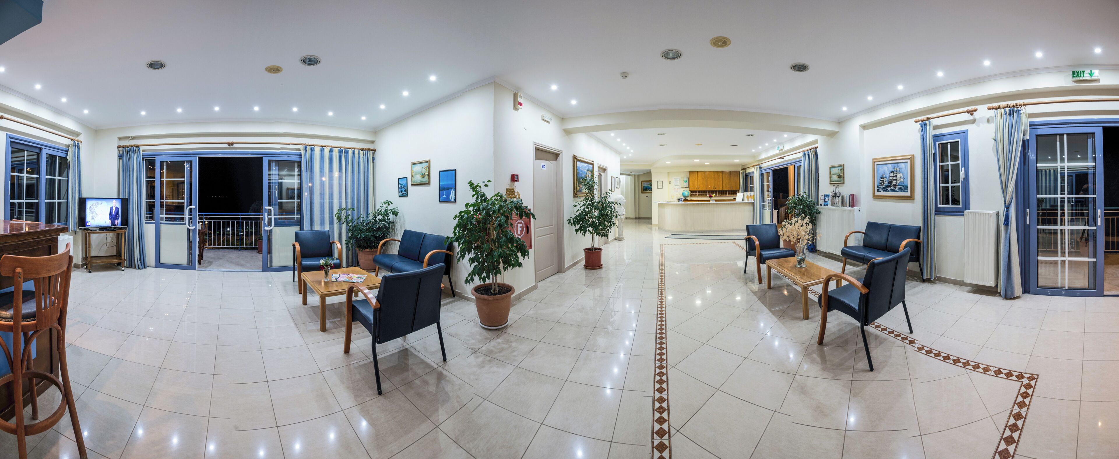 A hotel lobby with seating areas, potted plants, and a television.