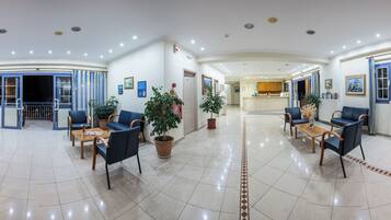 A hotel lobby with seating areas, potted plants, and a television.