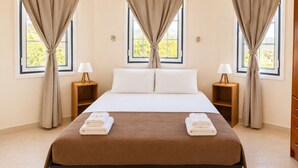 A hotel room with a large bed, two bedside tables with lamps, and curtains on three windows. - Cliff Bay Hotel by GHH (Aktio-Vonitsa)