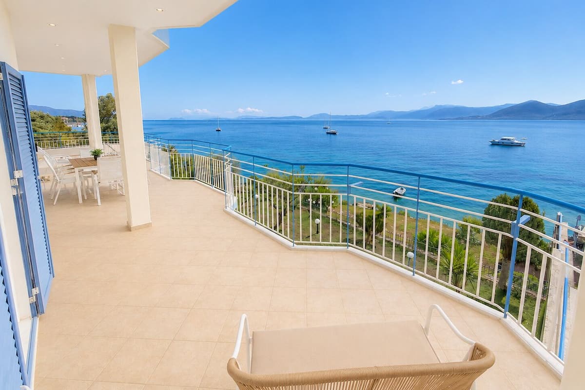 A balcony with a view of the sea, a dining area, and a wicker chair.