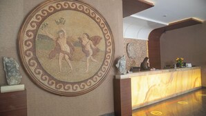 Un área de recepción con un muro de mosaico, un mostrador de recepción y una escultura de piedra.