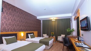 Habitación de hotel con dos camas, un escritorio con silla, televisor y ventana con cortinas.