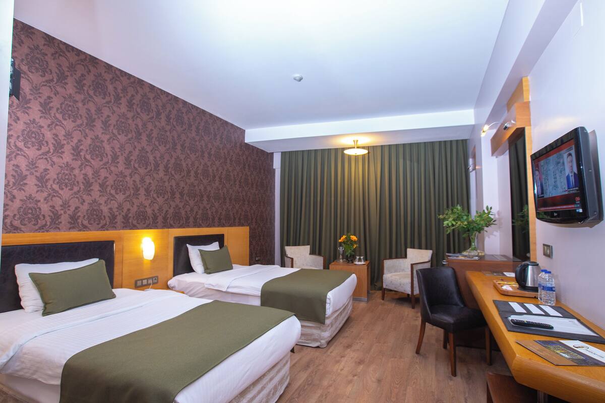 A hotel room with two beds, a desk with a chair, a television, and a window with curtains.