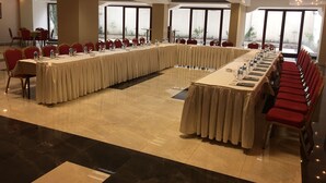 Un salón de conferencias con una larga mesa, sillas rojas y ventanas amplias.