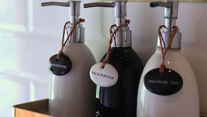 Une étagère contenant trois bouteilles de produits de toilette, étiquetées « shampoing », « après-shampoing » et « gel douche ».