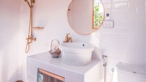 Une salle de bain avec un lavabo blanc, un miroir rond, une douche et des toilettes.