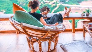 Une personne se détend dans un fauteuil en osier, avec une vue sur un paysage verdoyant et luxuriant.