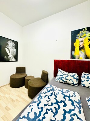 A modern bedroom with a bed, two ottomans, a red headboard, and two wall-mounted artworks. - Bright 4BR Apt for 8 Near FAC Platz (Vienna)