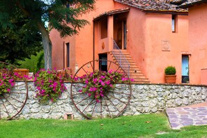 Um edifício rústico com parede de pedra, uma grande roda e flores cor-de-rosa.