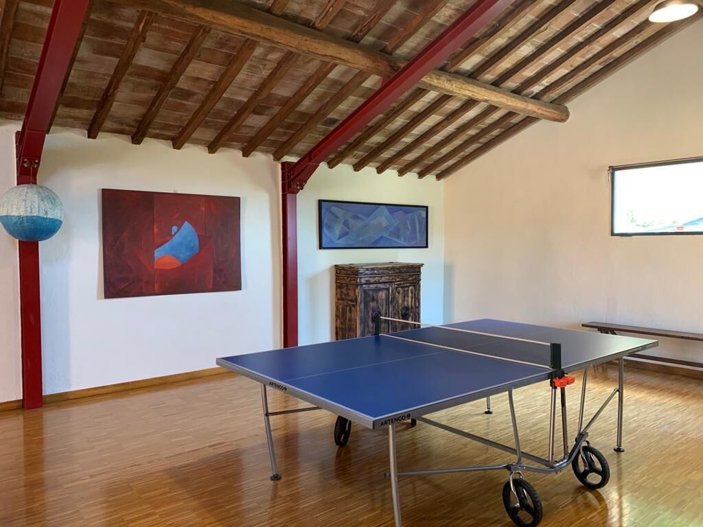 Una mesa de ping pong en una habitación con pisos de madera, una viga de techo roja y arte abstracto en las paredes.