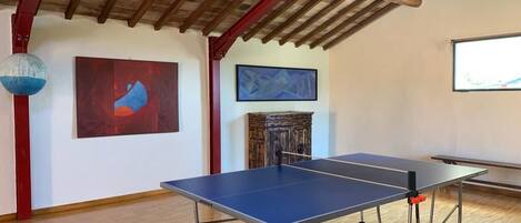 Una mesa de ping pong en una habitación con pisos de madera, una viga de techo roja y arte abstracto en las paredes.