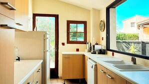 Una cocina compacta con armarios de madera, lavavajillas integrado, un ventanal con vistas al exterior y una pequeña ventana sobre el fregadero.