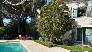 Una piscina con sillas de descanso, un comedor y un gran árbol en un patio.