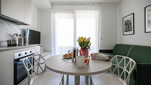 A modern kitchen with a dining table, chairs, a green sofa, and a window with curtains. - Italianway Comfort - Pasolini 8/G A (Milan)