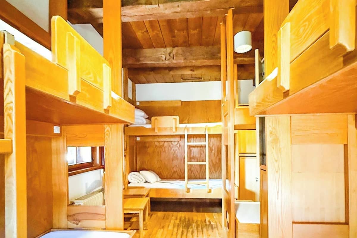 Una cabaña con literas de madera, un pasillo central y piso de madera.