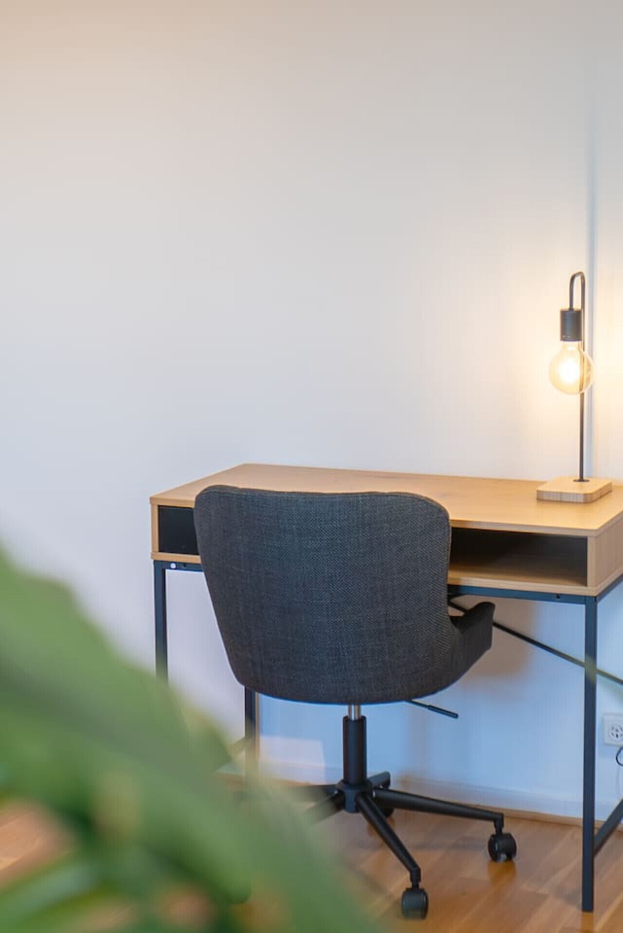Ein moderner Schreibtisch mit Stuhl, Schreibtischlampe und Computerbildschirm.