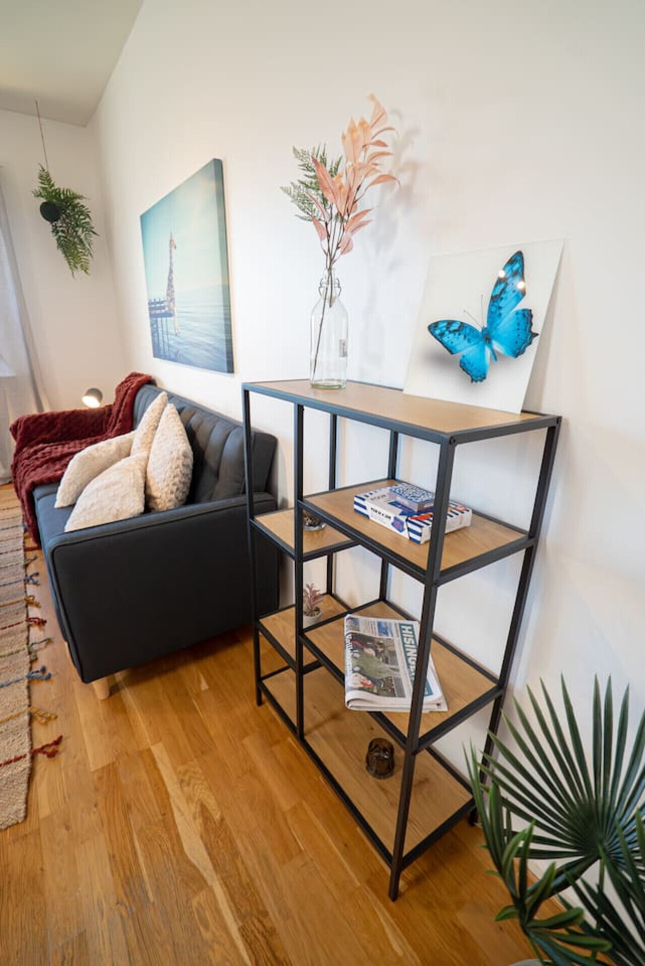 A living room with a black sofa, a wooden coffee table, a bookshelf, and a painting of a blue butterfly.