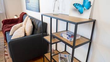 A living room with a black sofa, a wooden coffee table, a bookshelf, and a painting of a blue butterfly.