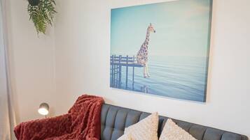 Un salon avec un canapé gris foncé, un plaid rouge et un tableau représentant une girafe accroché au mur.