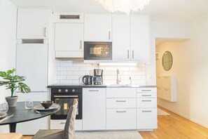 A modern kitchen with white cabinetry, a black stove, a microwave, and a coffee maker.