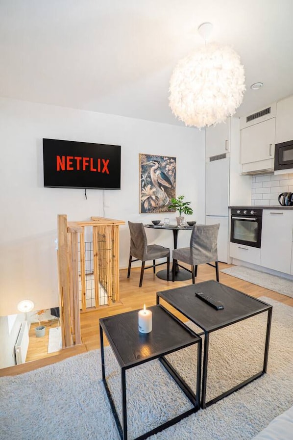 A modern living room with a flat-screen TV, a dining area, and a kitchen.