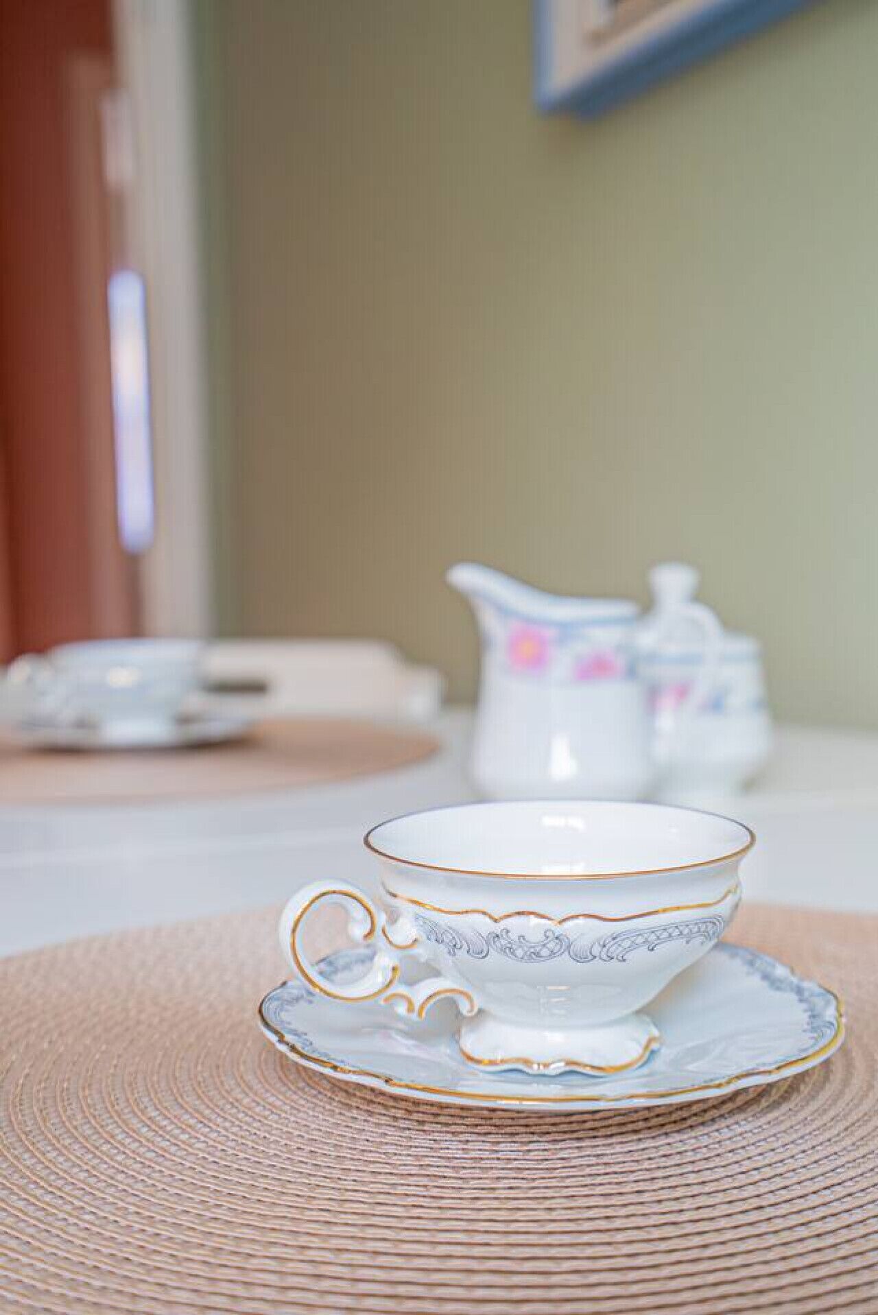Une table blanche ornée d’un service à thé décoratif, comprenant une tasse et une soucoupe, posé sur un set de table en fibres tressées.