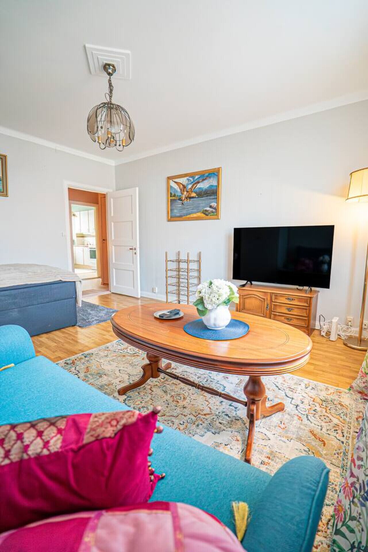Een woonkamer met een ronde houten salontafel, een blauwe bank, een televisie en een schilderij aan de muur.