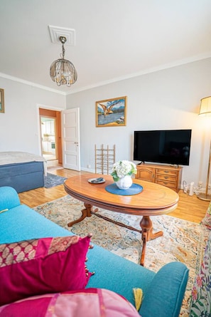 Een woonkamer met een ronde houten salontafel, een blauwe bank, een televisie en een schilderij aan de muur.