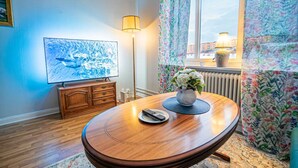 Una stanza con un tavolo da pranzo in legno, una televisione appesa al muro, una lampada e una finestra con tende.