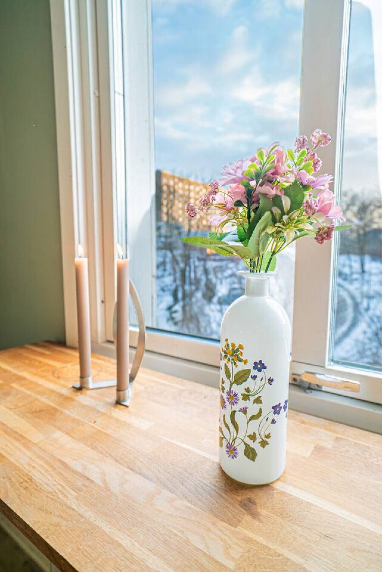 En hvid vase med blomstermønstre på en træoverflade nær et vindue.
