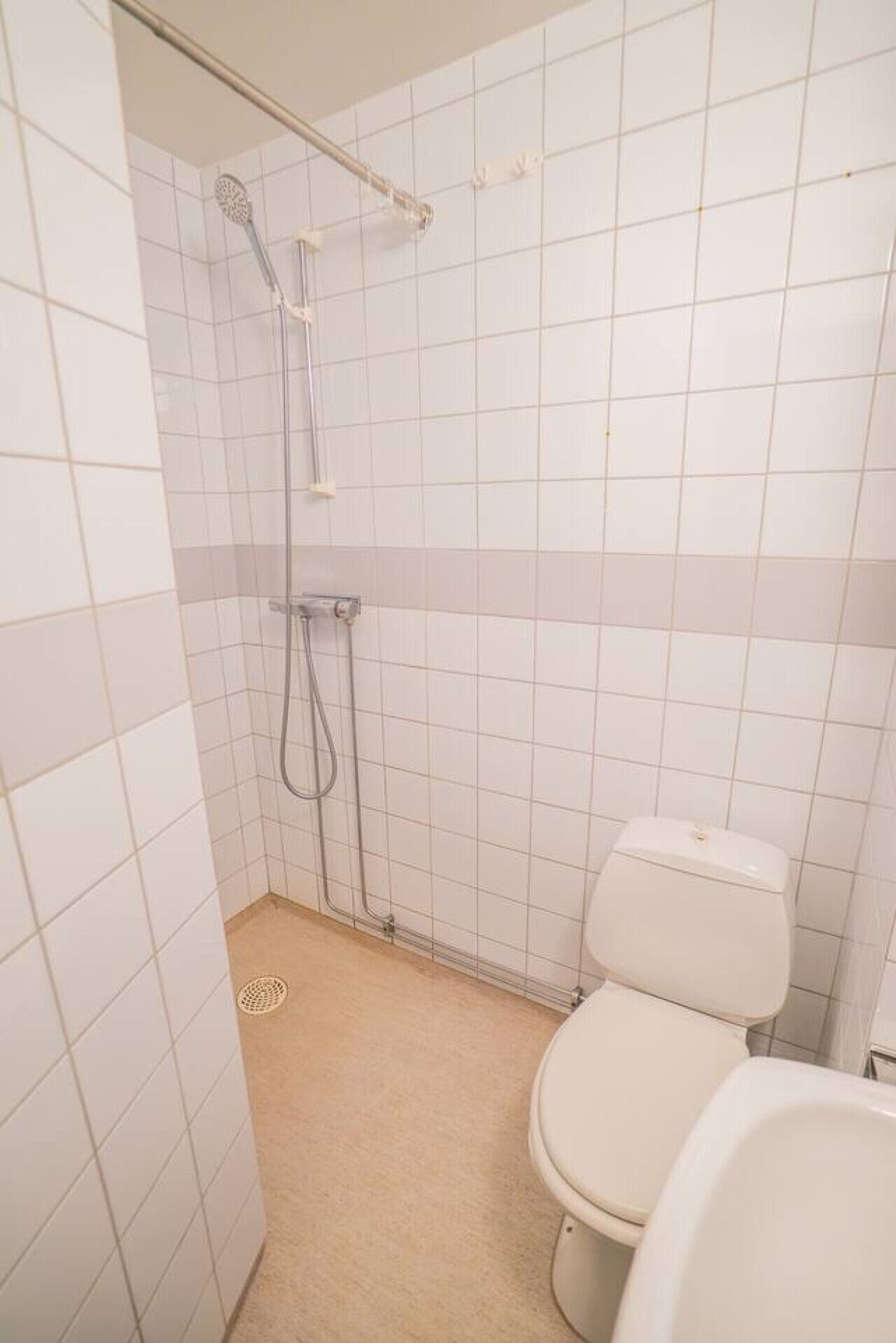 Ein kleines Badezimmer mit Fliesen, einer Dusche, einer Toilette und einem sichtbaren Abfluss.