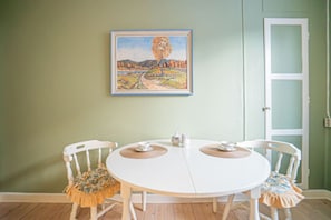 Een eetruimte met een ronde tafel, twee stoelen, een schilderij aan de muur en een deur.