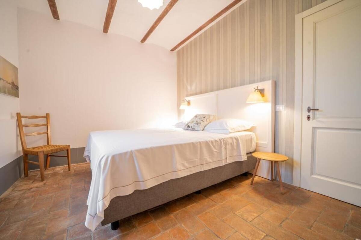 A bedroom with a bed, a chair, a bedside table, and a door.