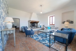 Una sala de estar con chimenea, sillones azules, una mesa de centro y alfombras estampadas.