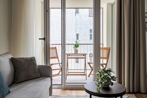 Ein modernes Wohnzimmer mit einer Couch, einem kleinen Tisch mit einer Pflanze und einem Balkon mit zwei Stühlen und einem Topf mit einer Pflanze.