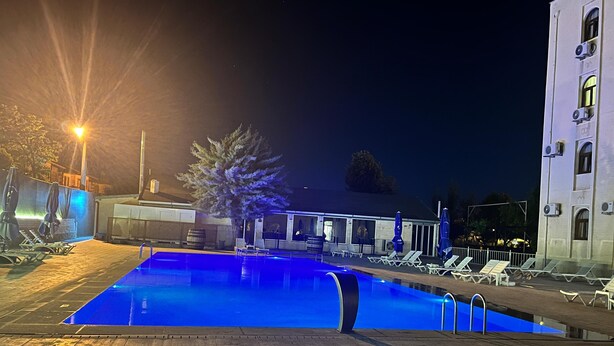 Una piscina con lettini e ombrelloni, un edificio con diverse finestre e un albero.