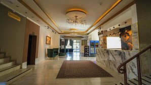 Una hall d'albergo con un lampadario, una reception, un'area salotto e una scala.