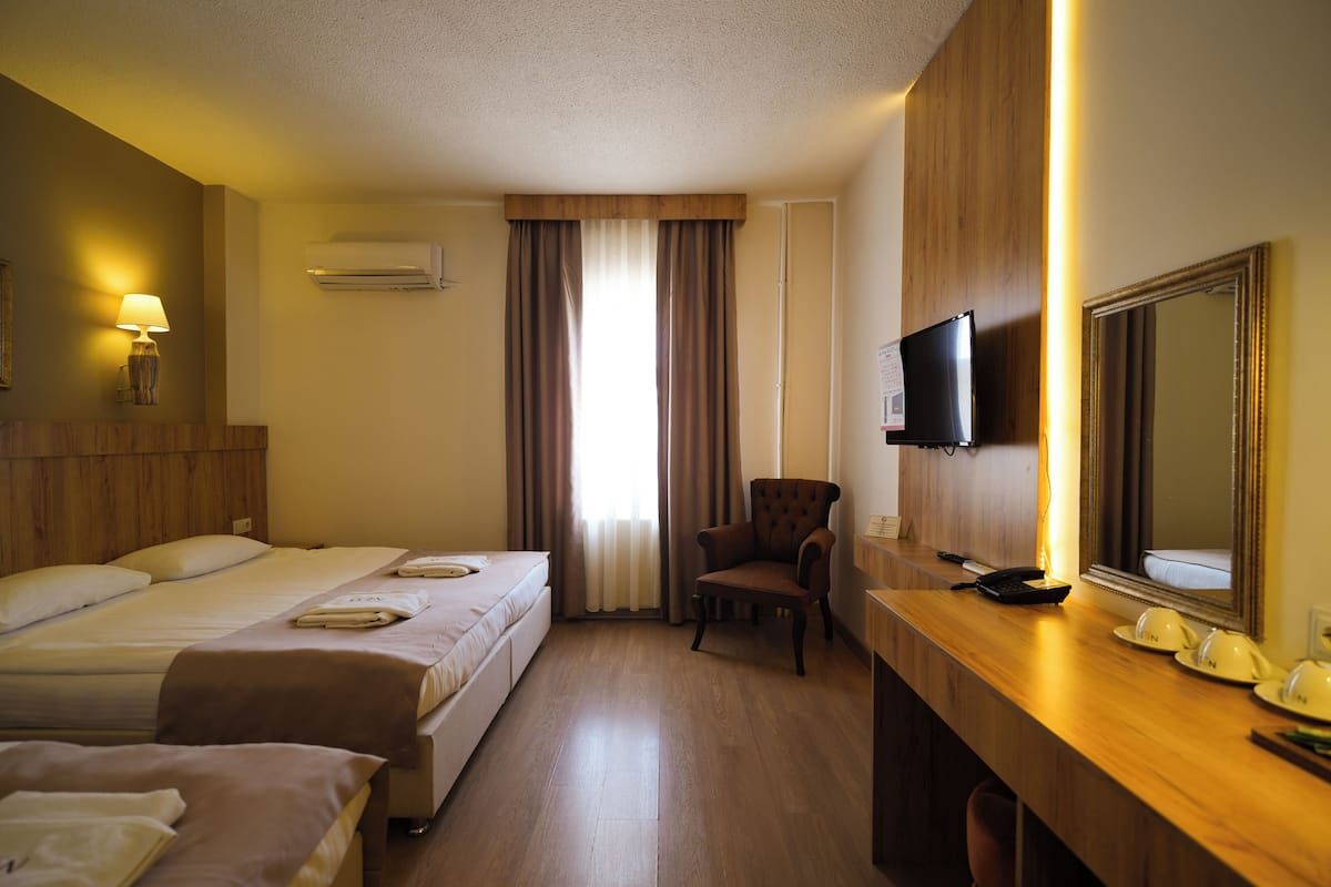 A hotel room with two beds, a desk with a flat-screen TV, a chair, and a large mirror.
