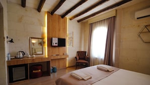 Camera d'albergo con soffitto in legno, un letto con copriletto beige, una sedia, una scrivania con uno specchio e una TV a parete.