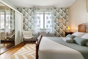 Een slaapkamer met een bed, een stoel, een spiegel en een raam met gordijnen.