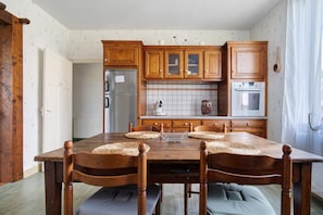 Uma mesa de jantar de madeira com quatro cadeiras, uma cozinha com armários de madeira e uma geladeira.