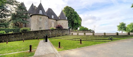 Un castello con un vialetto lastricato che conduce al suo ingresso, circondato da un muro di pietra e vegetazione.