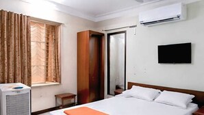 Habitación de hotel con cama, ventilador de techo, aire acondicionado, televisión y ventana con cortinas.