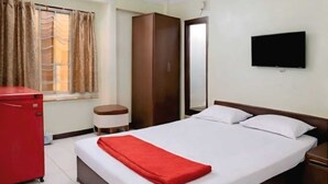 Habitación de hotel con cama, un armario rojo, ventilador de techo, televisión y ventana con cortinas.