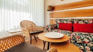 A room with a wicker chair, a round table, a floral sofa, and a wooden headboard. - Hotel Hasselhof Garni 4 Sterne (Braunlage)
